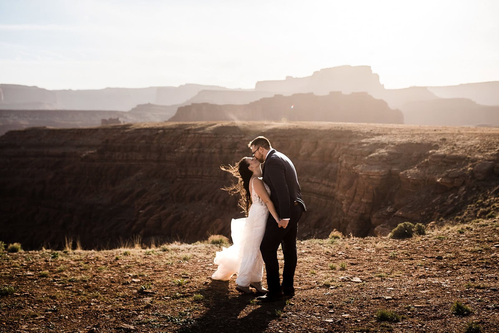 Newlyweds kissing at the edge of a canyon during their elopement ceremony.